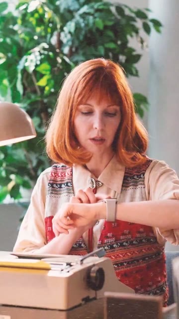 Standbild aus Clip 06: Frau am Schreibtisch schaut auf ihre Armbanduhr.
